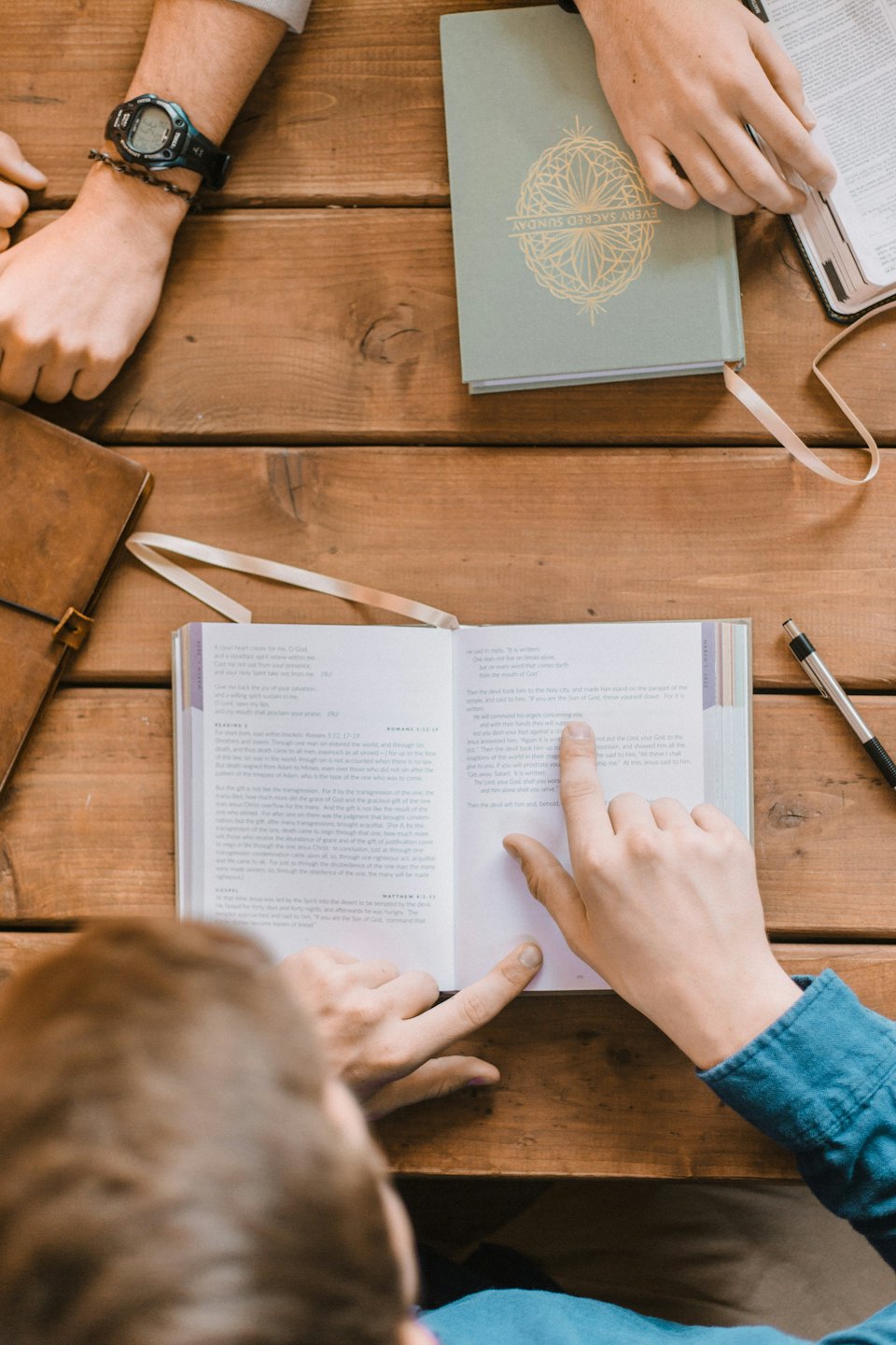 People discussing a book around a rustic wooden table.