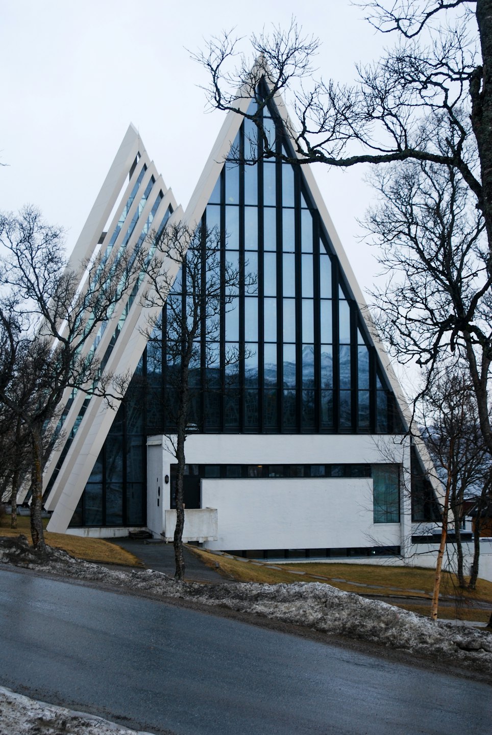 Modern church with triangular white facades stands beside a snowy road.